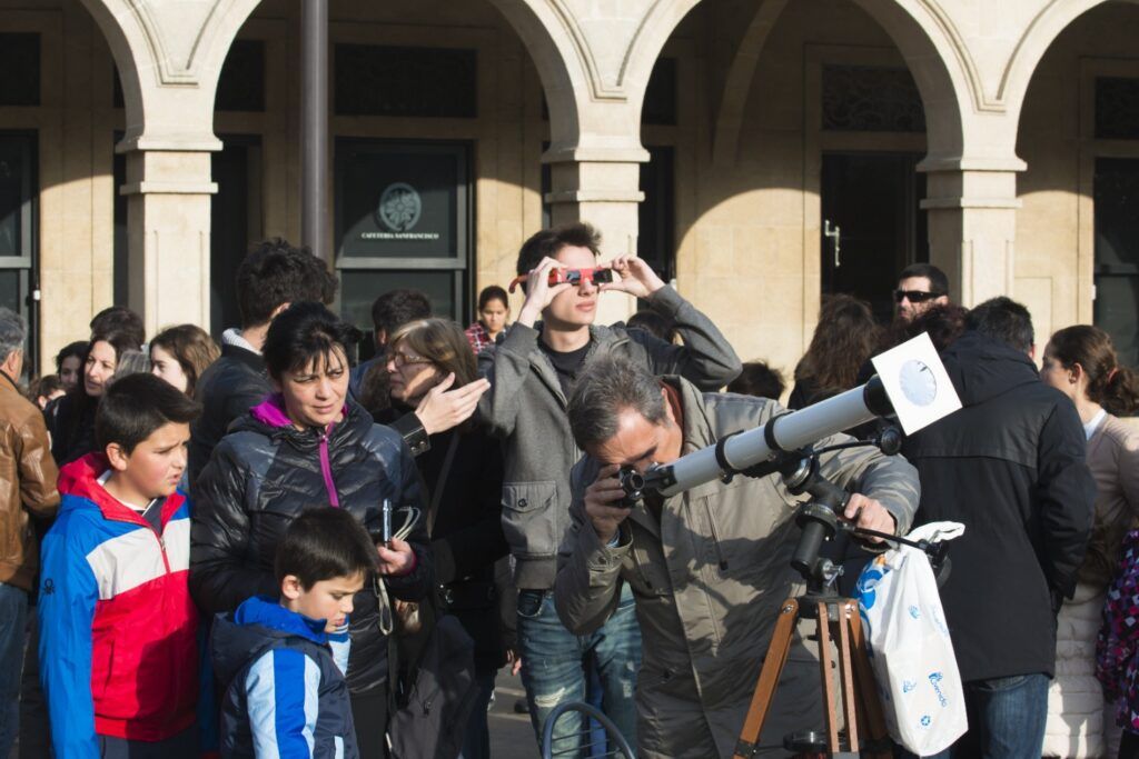 Personas reunidas en una plaza de España utilizando telescopios y gafas especiales para observar un eclipse solar.