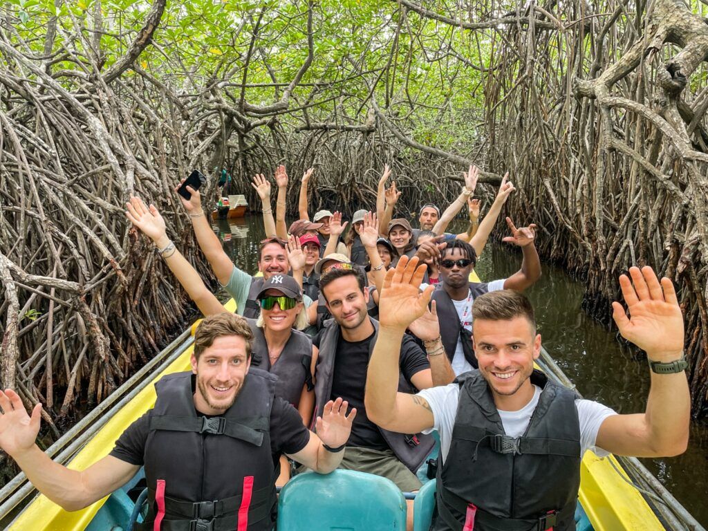 Un grupo de jóvenes sonrientes saludando a la cámara mientras navegan en barca por un manglar en Sri Lanka.
