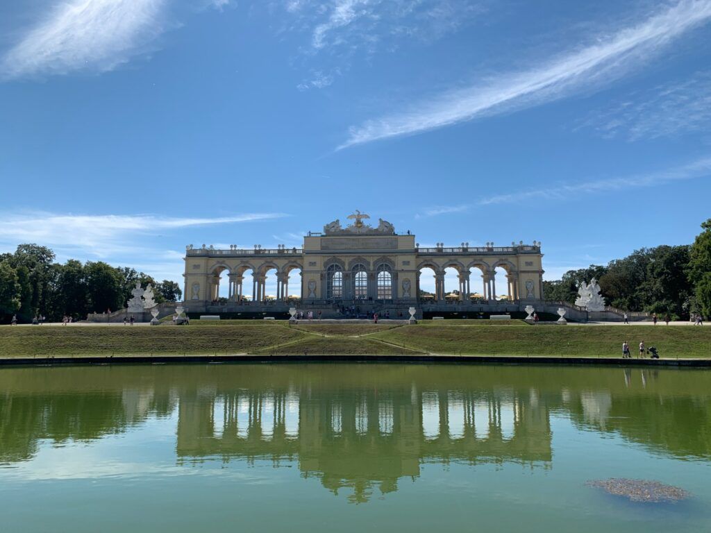 La Glorieta del Palacio de Schönbrunn en Viena se refleja simétricamente en un estanque bajo un cielo azul despejado.