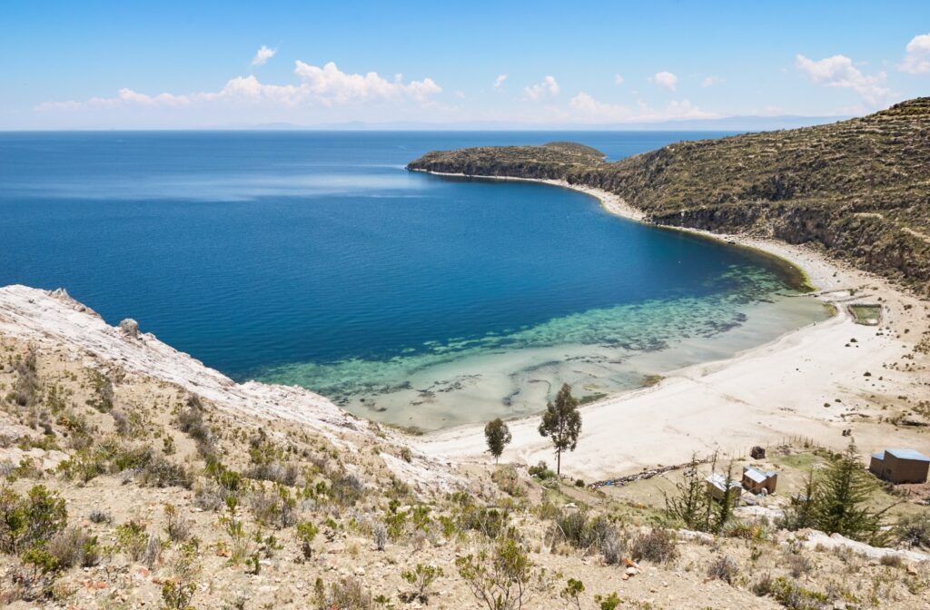 Vista panorámica de la bahía de Challapampa en la Isla del Sol, con playas de arena blanca y aguas cristalinas bajo un cielo azul.